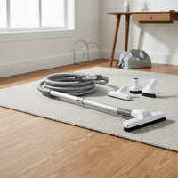 a central vacuum accessories and attachment kit: deluxe hose, hard floor brush, telescopic wand, upholstery tool, dusting brush, crevice tool, wall hose hanger and storage bag shown in a clean home office with a low-pile rug and oak flooring