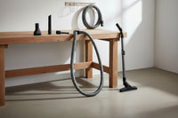 a garage central vacuum basic attachment kit: hose, upholstery brush, dusting brush, crevice tool and wall hose hanger shown in a workshop garage with concrete floors and a workbench